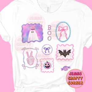 May include: White t-shirt featuring colorful Halloween-themed graphics. Designs include a ghost, a bat, a pumpkin, a bow, and a candy, all within decorative frames. The text "BOO" is also displayed.