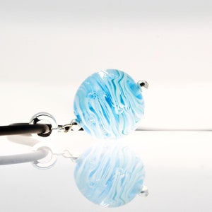 Puede incluir: Un orbe de vidrio azul y blanco con una cadena plateada unida. El orbe tiene un patr&oacute;n de remolino y parece tener burbujas de aire atrapadas en su interior.