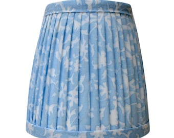 Puede incluir: Una pantalla de lámpara azul claro con un patrón floral blanco. La pantalla es plisada y tiene un borde festoneado.