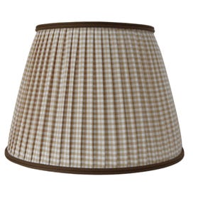 May include: A pleated lampshade with a tan and white checkered pattern. The lampshade has a brown trim at the top and bottom edges. The lampshade is a classic design for home lighting.