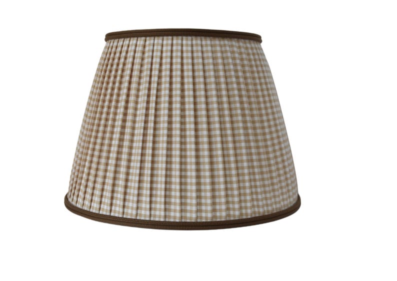 May include: A pleated lampshade with a tan and white checkered pattern. The lampshade has a brown trim at the top and bottom edges. The lampshade is a classic design for home lighting.