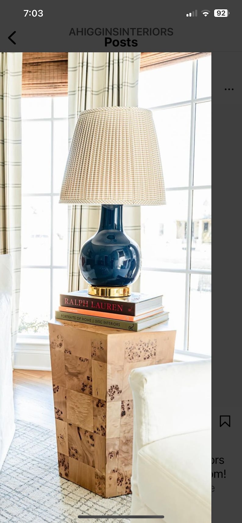 May include: A navy blue lamp with a woven beige shade sits atop a stack of books on a wooden side table. The lamp has a gold base and a spherical body. The books include "RALPH LAUREN" and "PORTRAITS OF HOME".