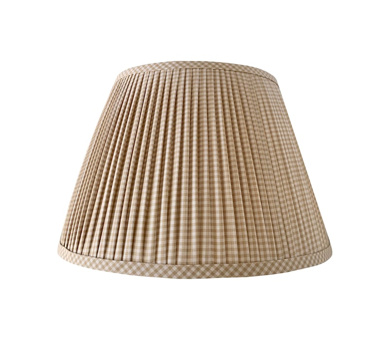 May include: A beige and white plaid lampshade with a pleated design. The lampshade has a classic, tapered shape and a decorative trim at the bottom. The fabric has a gingham pattern.
