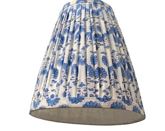 May include: A white lampshade with blue floral print and pleated fabric. The lampshade is a classic style with a wide, round bottom and a narrow top.