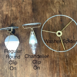 May include: Three lamp shade components are displayed against a wood background. The items include a regular round clip-on shade, a chandelier clip-on shade, and a washer spider. The text on the image reads "Regular Round Clip On", "Chandelier Clip On", and "Washer Spider".