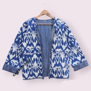 May include: A blue and white patterned quilted jacket with a button closure and two pockets. The jacket has a striped lining and is made of cotton.