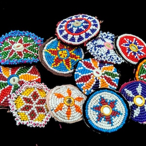 Op de afbeelding: Een verzameling kleurrijke, ronde, kralenversieringen met een stervormig ontwerp. Elk ornament heeft een kleine, ronde knop in het midden.