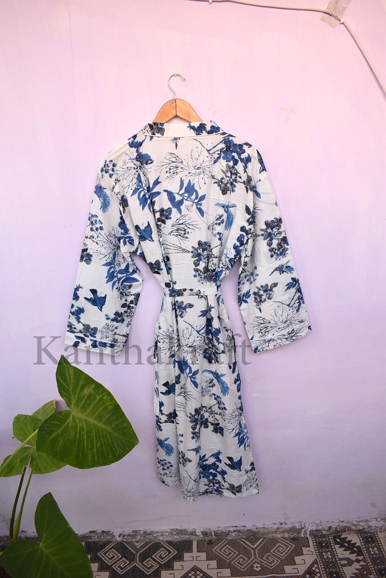 May include: White cotton robe with a blue floral print featuring birds and leaves. The robe has a tie belt and long sleeves.