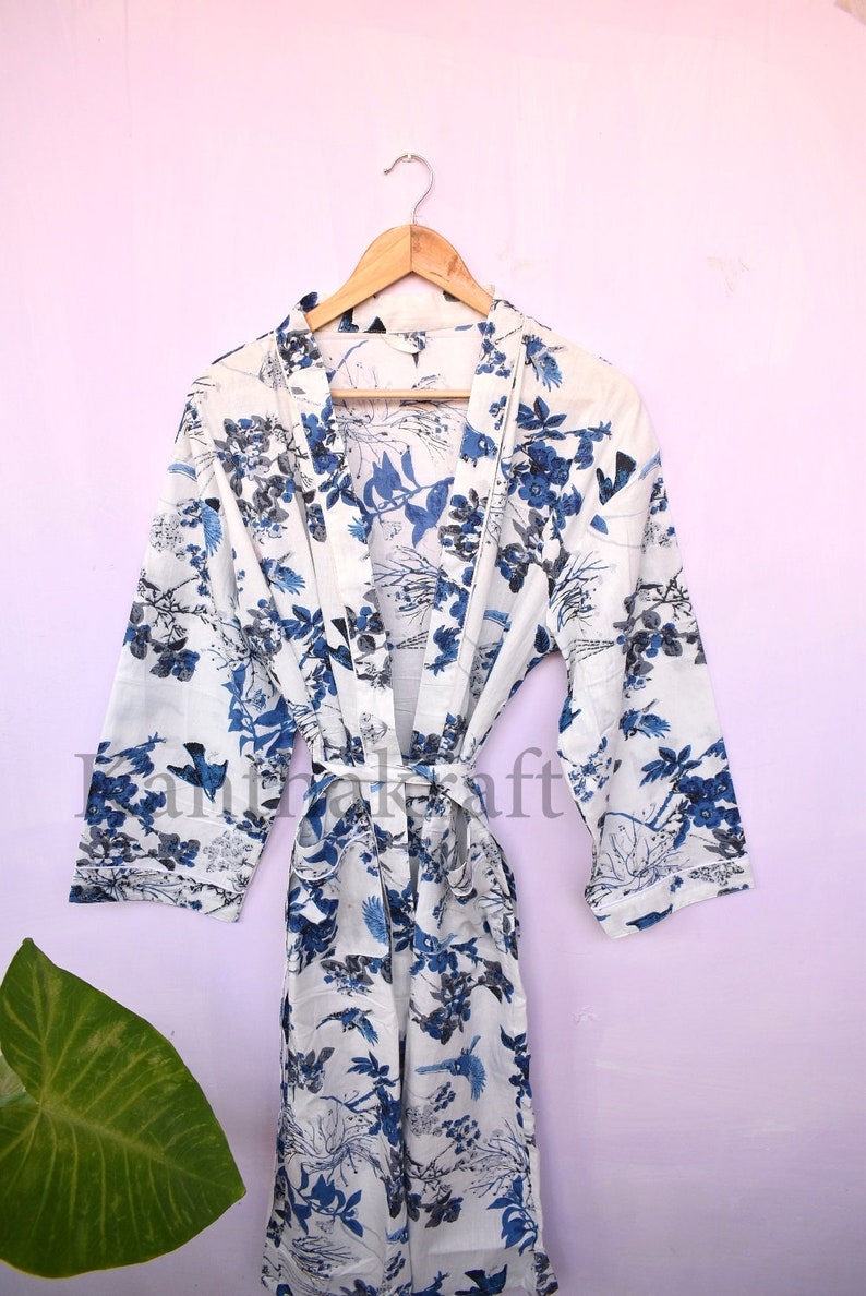 May include: White cotton robe with a blue floral print featuring birds and branches. The robe has a tie belt and long sleeves.