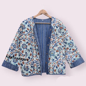 Peut inclure: Une veste matelassée bleu et blanche avec un motif floral. La veste est doublée de rayures et se ferme par des boutons. Le texte "KANTHAKRAFT" est brodé sur la manche.