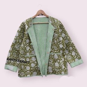 Könnte beinhalten: Eine reversible, gesteppte Jacke in Grün und Weiß mit einem Blumenmuster auf der einen Seite und einem Streifenmuster auf der anderen. Die Jacke hat einen Knopfverschluss und zwei Taschen. Der Text "KANTHAKRAFT" ist auf dem linken Ärmel gestickt.