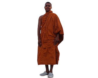 May include: A Buddhist monk wearing a traditional saffron-colored robe. The robe is long and flowing, and the monk is standing with his hands clasped in front of him.