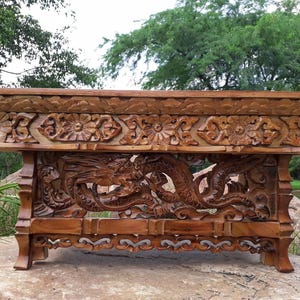 Può includere: Un tavolo da altare rettangolare in legno caratterizzato da intricati motivi floreali intagliati a mano lungo il bordo superiore e un rilievo dettagliato di un drago che si snoda tra le nuvole sul pannello centrale, con quattro gambe intagliate.