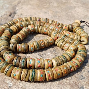 May include: A string of prayer beads made of bone with intricate designs in shades of brown, green, and blue.