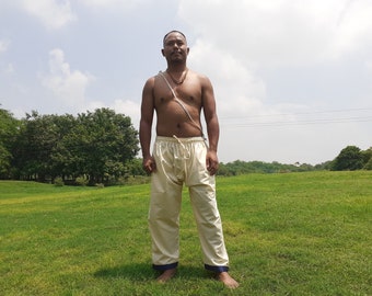 May include: A man wearing a pair of white pants with a blue trim at the bottom. He is standing in a grassy field with trees in the background.