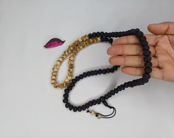 May include: Two beaded necklaces. One is black, the other is tan. The tan necklace has skull-shaped beads. The black necklace is being held by a hand. The necklaces are on a white surface.