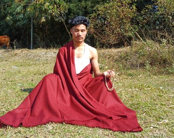 May include: A deep maroon, rectangular wool shawl draped over the shoulders and legs, featuring a smooth, solid-colored fabric with a fringed edge. The garment is worn over a white sleeveless undershirt and is held in place while seated.
