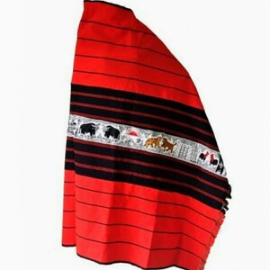 May include: A red and black woven shawl with a white embroidered band featuring animals and a sun. The shawl has fringe on the bottom edge.