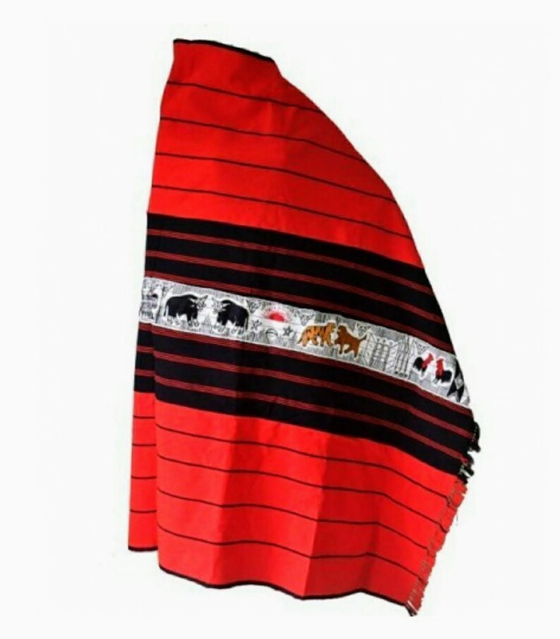 May include: A red and black woven shawl with a white embroidered band featuring animals and a sun. The shawl has fringe on the bottom edge.