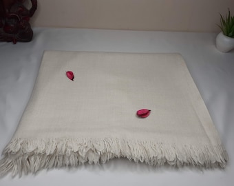 May include: A white, fringed throw blanket with a subtle texture. Two small, pink flower petals are placed on the blanket.
