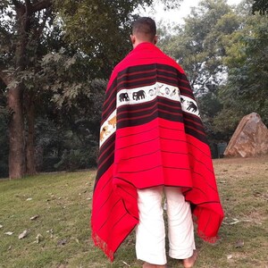May include: A person wearing a red and black woven shawl with a pattern of elephants and tigers. The shawl has a fringe border and is draped over the person's shoulders.