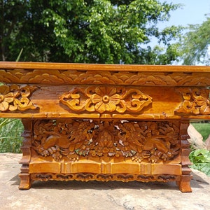 May include: A wooden altar table with intricate carvings of flowers and mythical creatures. The table is made of a rich, golden brown wood and has a rectangular top.