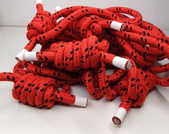 May include: Red and black rope with white tips, tied in knots. The rope is coiled and arranged in a pile.