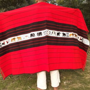 May include: A red and black woven blanket with a white stripe featuring embroidered animals and symbols. The blanket has fringe on the edges.