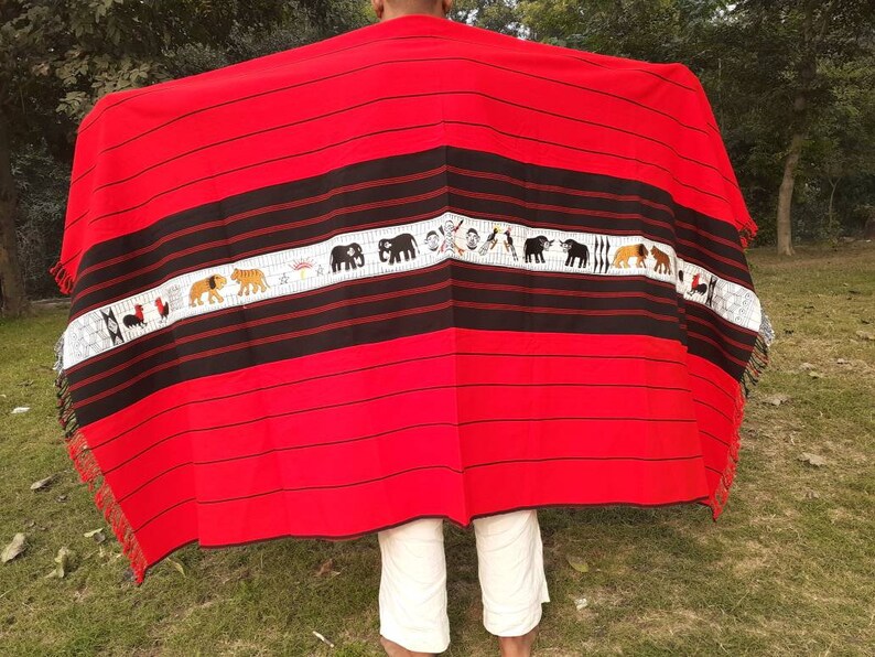 May include: A red and black woven blanket with a white stripe featuring embroidered animals and symbols. The blanket has fringe on the edges.