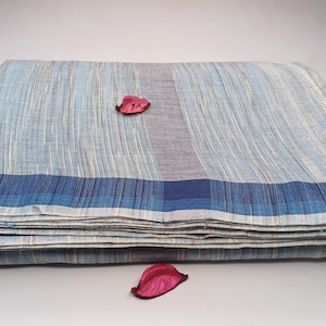 Puede incluir: Una tela de rayas blancas y azules claras doblada con un borde azul. La tela tiene un brillo sutil y está doblada cuidadosamente.