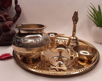 May include: A brass puja thali set with a decorative pot, a bell, a diya, and a small bowl. The set is on a round, ornate tray.
