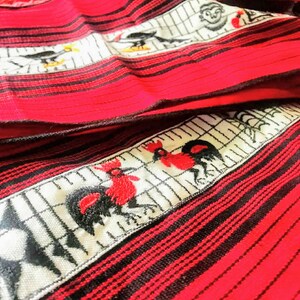May include: Red and black striped fabric with white embroidered designs of roosters and other birds. The fabric has a woven texture.