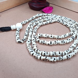 Peut inclure: Un collier mala en os blanc avec des marques noires sur chaque perle. Le collier est encordé avec un cordon noir et a un gland en os blanc.