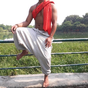 May include: A person wearing a white pair of loose-fitting trousers with a red scarf around their neck. The person is standing on a concrete surface with a green metal railing in front of them.
