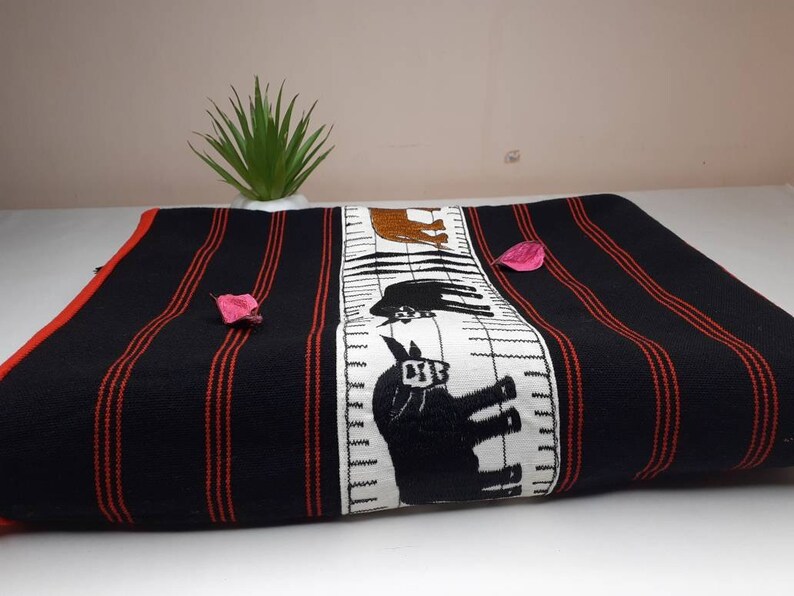 May include: Black and red striped fabric with a white panel featuring embroidered black animal silhouettes. The fabric is folded and displayed on a white surface.