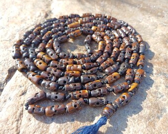 May include: A long strand of brown wooden beads with skull carvings. The beads are strung on a black cord and have a blue tassel at the end.