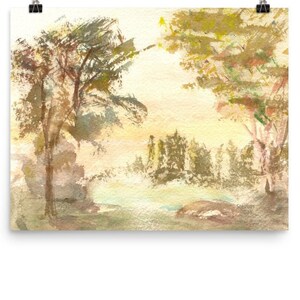 May include: Watercolor painting of a landscape featuring trees and foliage in shades of brown, green, and yellow. The artwork has a soft, blurred effect, with a light, airy feel. The painting is mounted on a white background and held by a black clip.