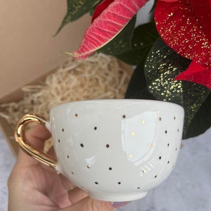 May include: White ceramic teacup with a gold handle and gold polka dots.