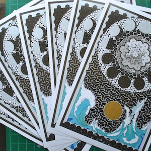 May include: A stack of eight black and white prints with a geometric design. The design features a circle with a repeating pattern of crescent moons and a central hexagon. The bottom print has a blue and white wave design with a gold sun.