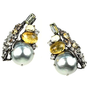 May include: A pair of silver earrings with a large gray pearl, yellow and clear gemstones, and a silver branch design.