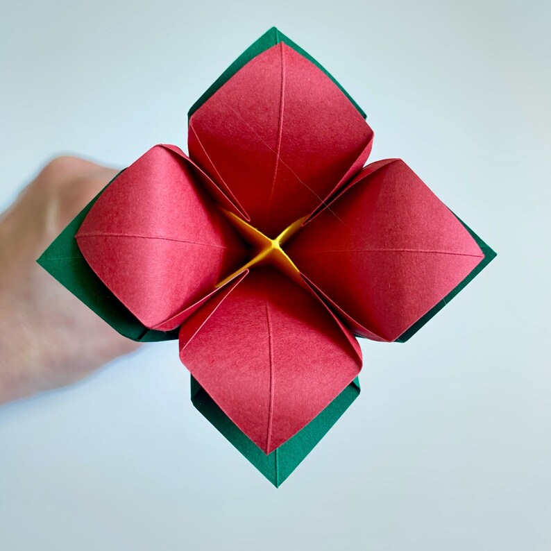 top view of one flower you make in this do-it-yourself origami kit , showing the red petals, dark green calyx and yellow center.
