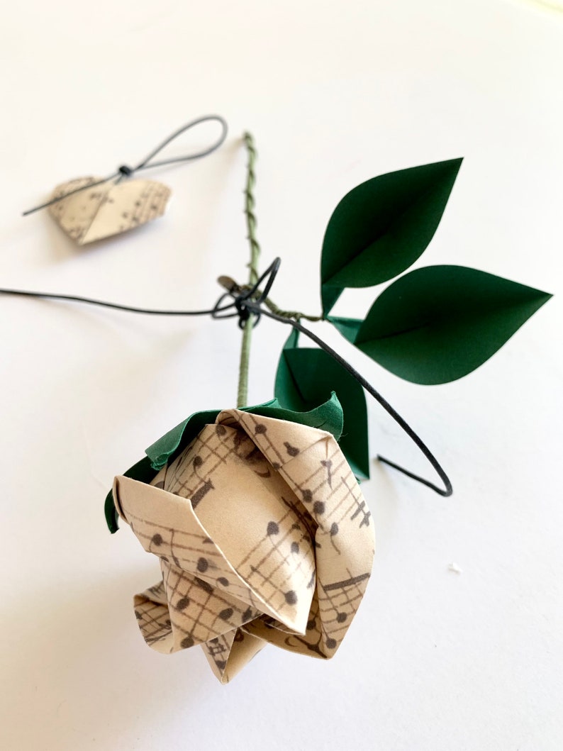 Another view of the Origami rose laying on a table besides an origami heart ornament made with the same musical sheets paper as the rose. The heart is an extra touch I add to orders who purchase gift wrapping at check out.