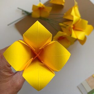 detail closer view of the process of making the origami flower you learn on this DIY kit, showing a yellow flower with the center in orange paper