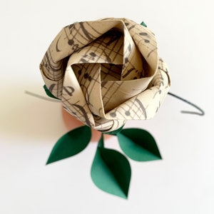 top view of the origami rose button, made out from a vintage looking paper of musical sheets. You can also see the three paper leaves of the rose below.