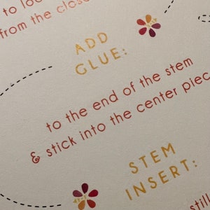 May include: Close-up of instructions for a craft project. The text reads "ADD GLUE: to the end of the stem & stick into the center piece" and "STEM INSERT:".