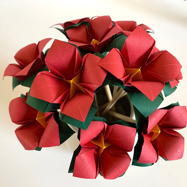 top view of a bunch of origami flowers in red paper, with yellow centers and dark green calyxes