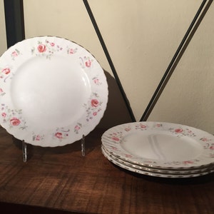 Peut inclure: Quatre assiettes en céramique blanche avec un motif floral rose et vert et un bord doré.