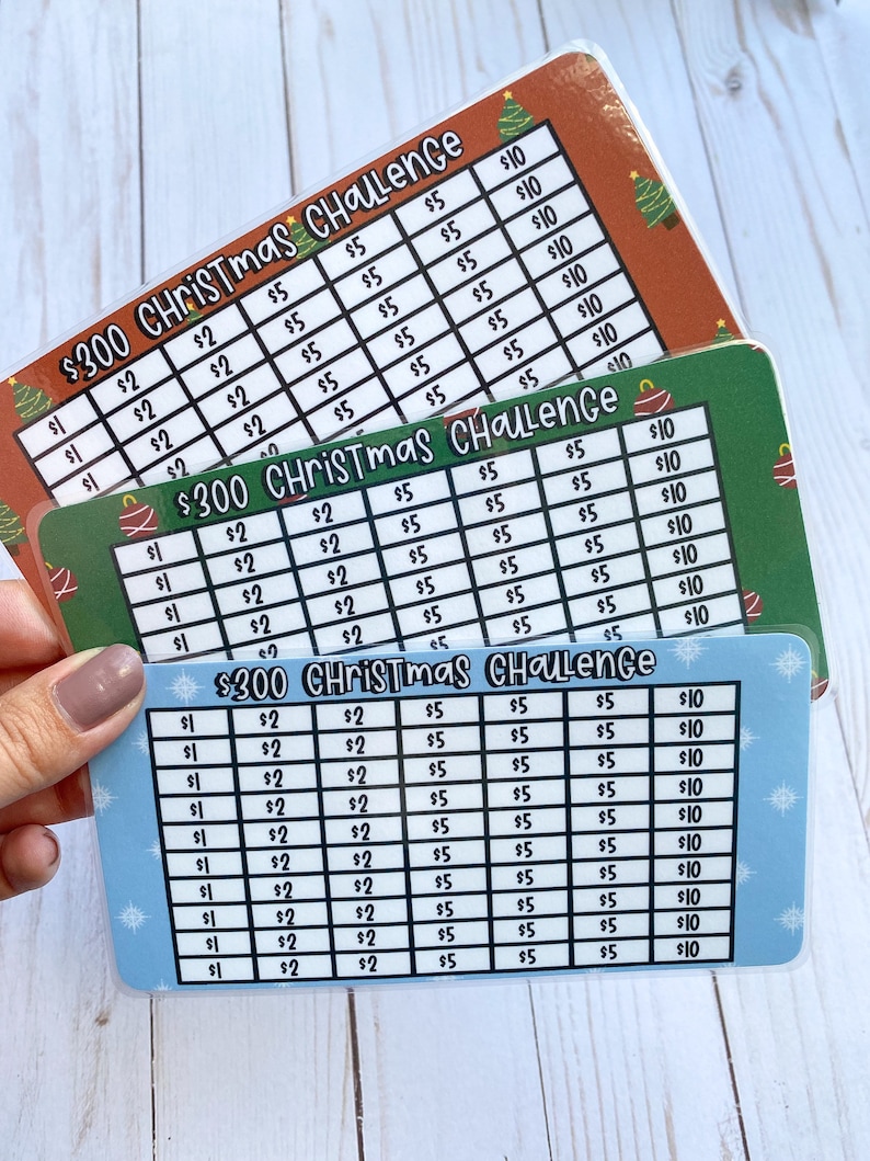 May include: Three different Christmas challenge cards with a blue, green, and orange background. Each card has a grid with dollar amounts from $1 to $10. The text "$300 Christmas Challenge" is printed on each card.
