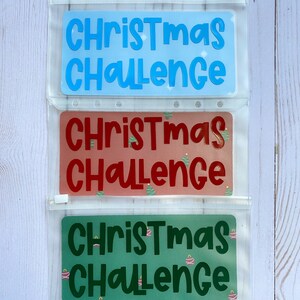 May include: Three clear plastic zippered pouches with different Christmas Challenge designs. The top pouch has a light blue background with white text. The middle pouch has a red background with white text and a green Christmas tree design. The bottom pouch has a green background with white text and a red Christmas ornament design.
