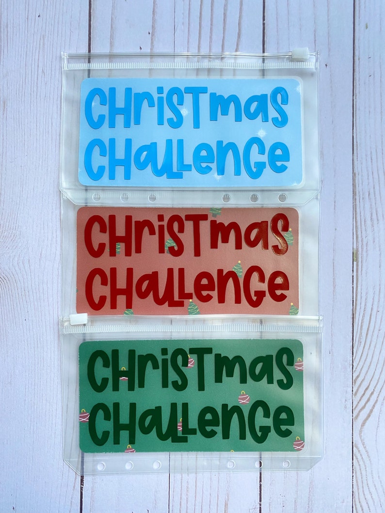 May include: Three clear plastic zippered pouches with different Christmas Challenge designs. The top pouch has a light blue background with white text. The middle pouch has a red background with white text and a green Christmas tree design. The bottom pouch has a green background with white text and a red Christmas ornament design.